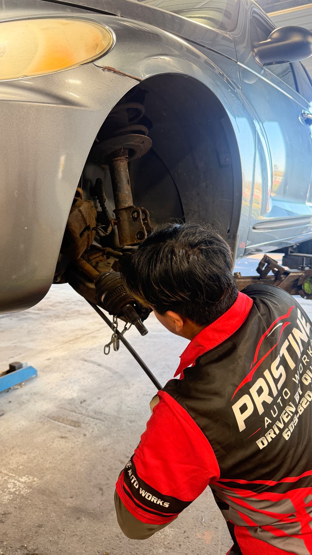 A Pristine Auto Works technician servicing a front suspension and CV axle